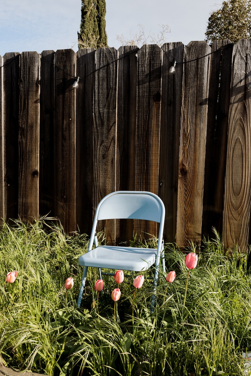 a blue chair sitting in tall grass next to a fence